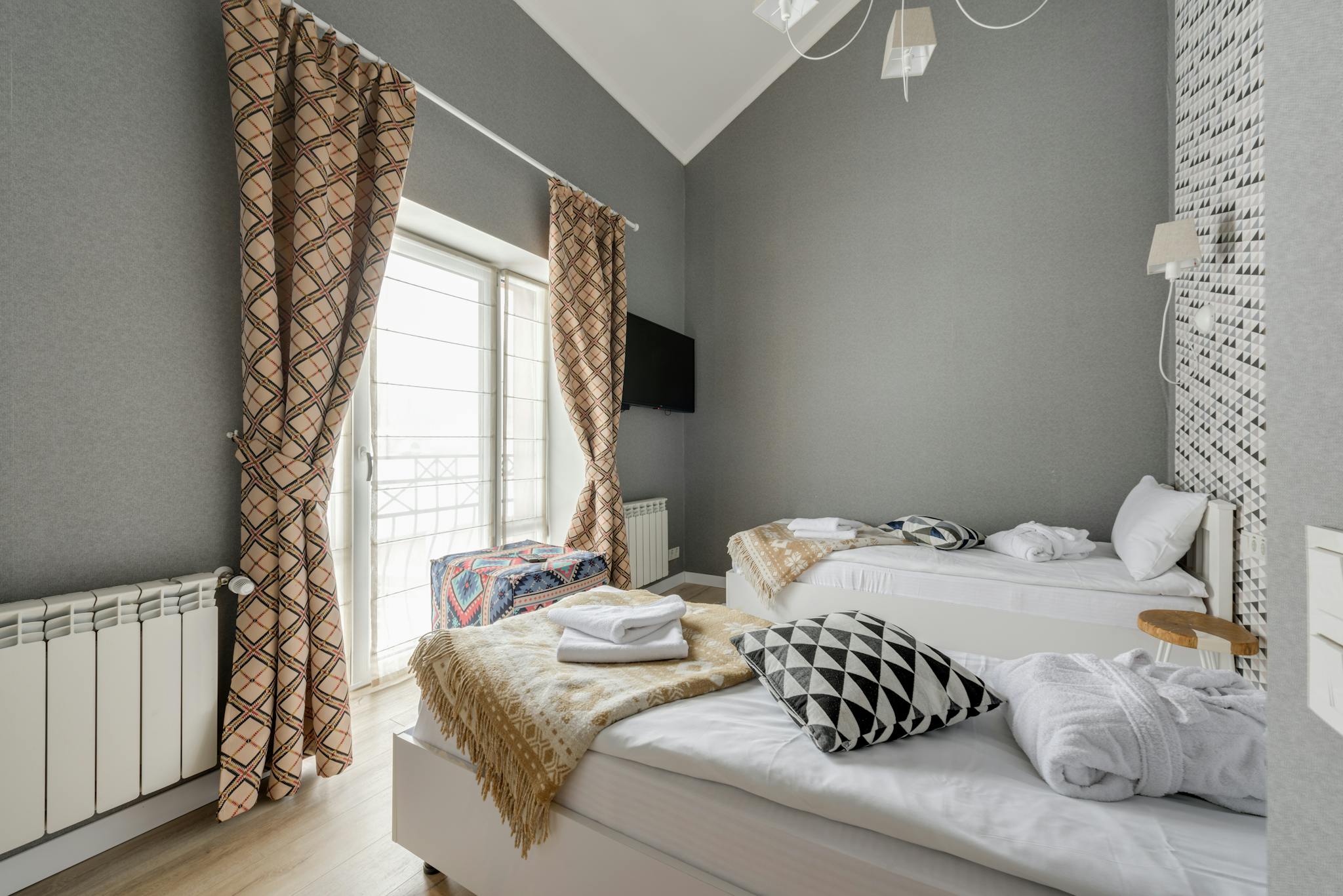 Stylish bedroom with twin beds, patterned curtains, and wall-mounted TV.